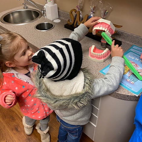 Two kids brushing a model of the teeth with giant fake toothbrush in dental office