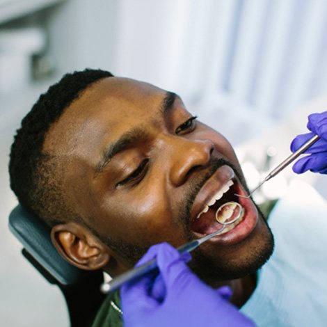 Dentist with blue gloves using tools to examine patient's teeth