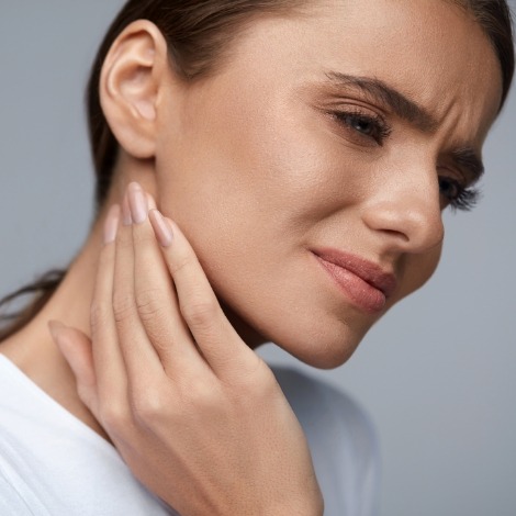 Woman holding the side of her jaw in pain before T M J treatment